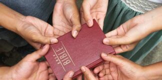 Hands holding a red Holy Bible together.