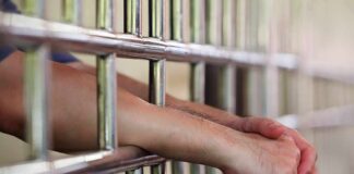 Hands gripping jail cell bars.