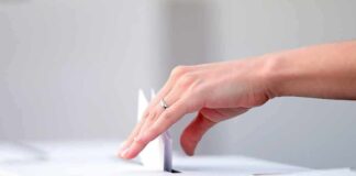 Hand placing paper in ballot box.