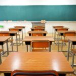 Classroom with wooden desks and empty green chalkboard.
