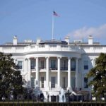 White House with American flag flying, daytime.