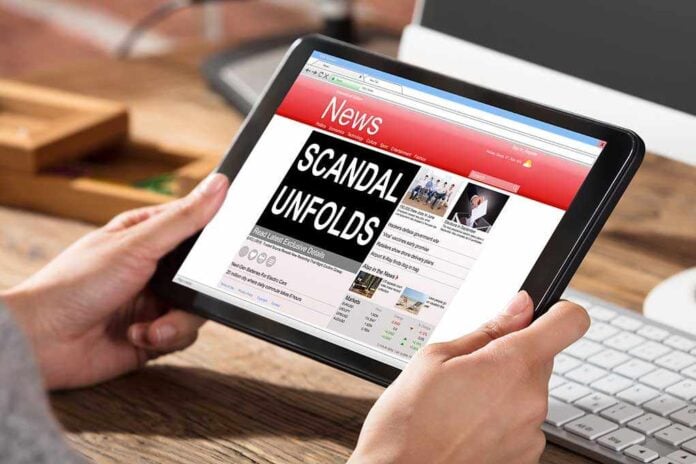 625950956 featured image Person holding tablet displaying news headline "Scandal Unfolds".