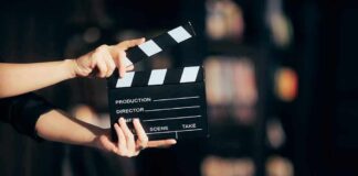 Hands holding a film clapperboard against a dark background.