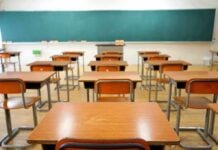 Classroom with wooden desks and empty green chalkboard.