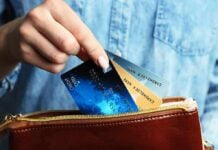 Hand holding credit cards over a brown purse.