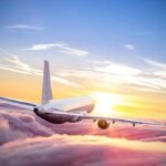 Airplane flying above clouds during vibrant sunset