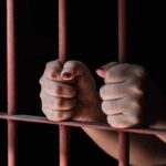 Hands gripping rusty prison bars in darkness