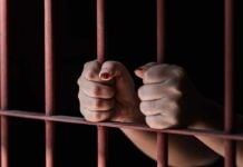 Hands gripping rusty prison bars in darkness