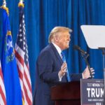 Person speaking at podium with flags in background