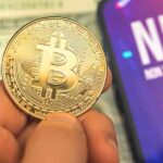 Person holding Bitcoin coin NFT text on screen