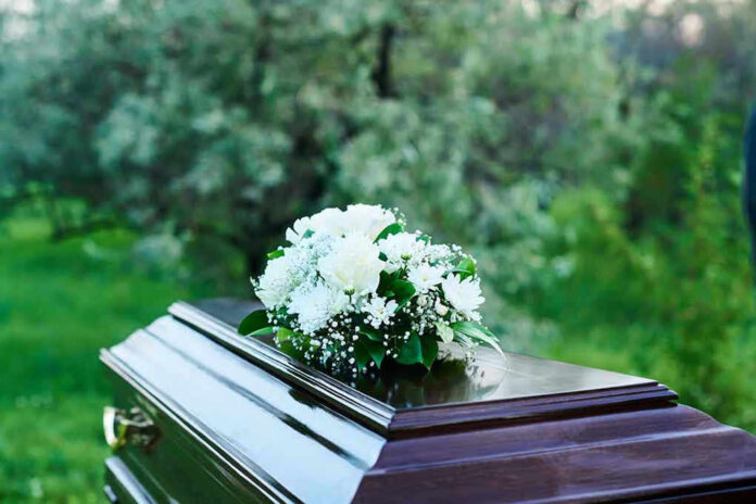 2361639877 Coffin with white flowers outdoors in green surroundings