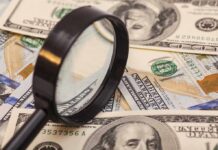 A magnifying glass resting on a pile of US dollar bills