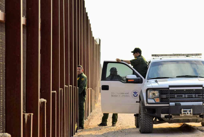 Border patrol agents near a tall metal fence