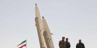 Military personnel beside missiles and Iranian flag