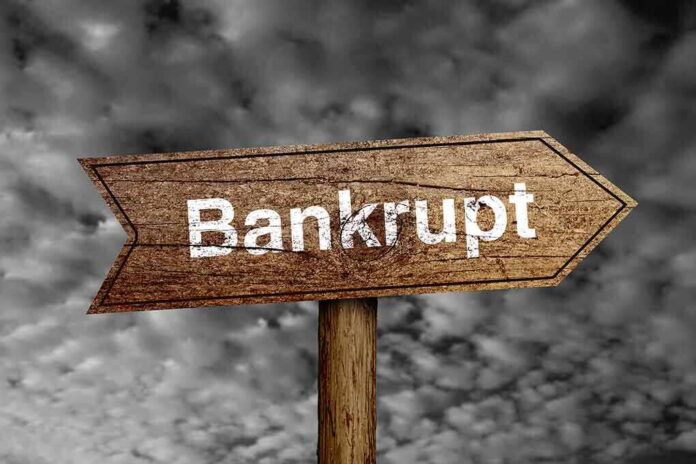 Wooden arrow sign pointing towards the word 'Bankrupt' against a cloudy background