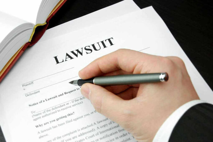 Hand holding pen, filling out lawsuit form.