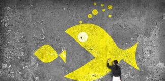 A woman painting a large yellow fish mural on a concrete wall