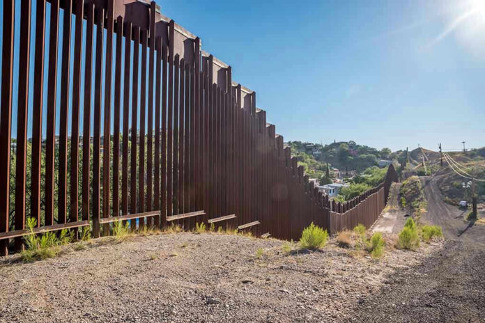 Tall metal border wall with rural landscape.