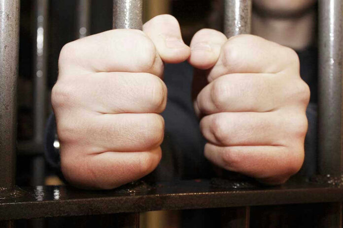 Hands gripping jail cell bars tightly.