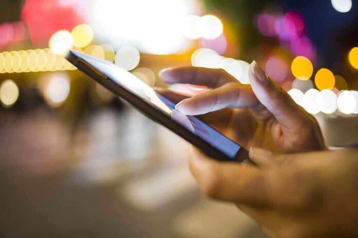 A persons hand using a smartphone in a city at night with blurred lights in the background