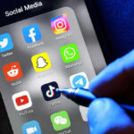 BIZARRE TikTok “Recruitment” Post Triggers Arrest Social media apps on phone screen with hand holding stylus.