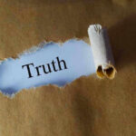 Ripped paper reveals word truth underneath brown surface