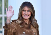 Melania Trump waving and smiling while wearing a stylish coat