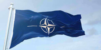 NATO flag waving against blue sky.