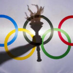 Shadow of torch over Olympic rings logo.