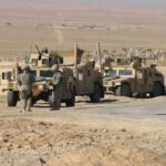 Soldiers beside military vehicles in a desert area.