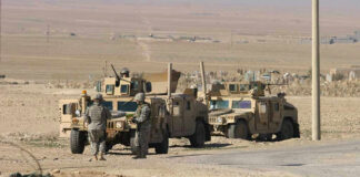 Soldiers beside military vehicles in a desert area.