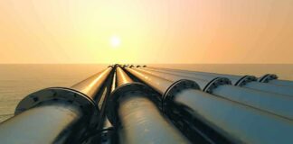 Industrial pipes extending towards the horizon over water during sunset