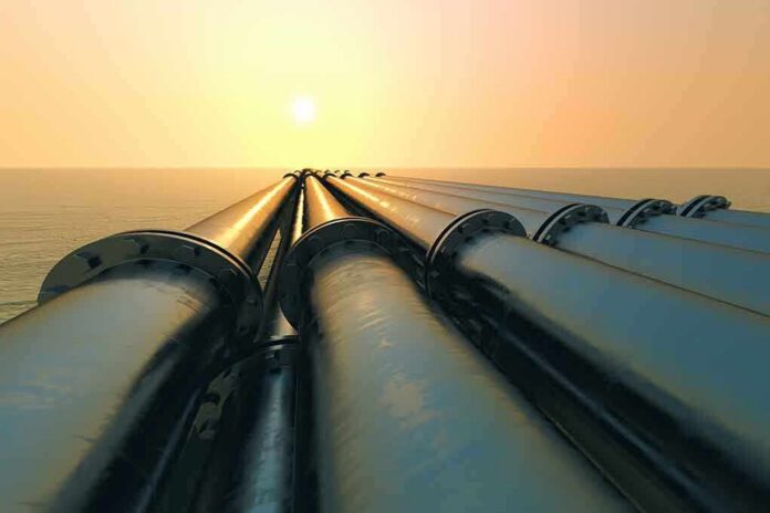 Industrial pipes extending towards the horizon over water during sunset