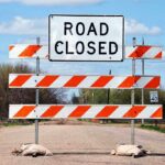 A Road Closed sign with orange and white barriers on a rural road