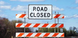 A Road Closed sign with orange and white barriers on a rural road