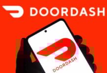 A hand holding a smartphone displaying the Doordash logo against a bright red background