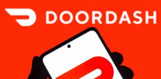 A hand holding a smartphone displaying the Doordash logo against a bright red background