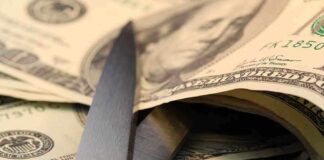 Scissors cutting through a stack of dollar bills