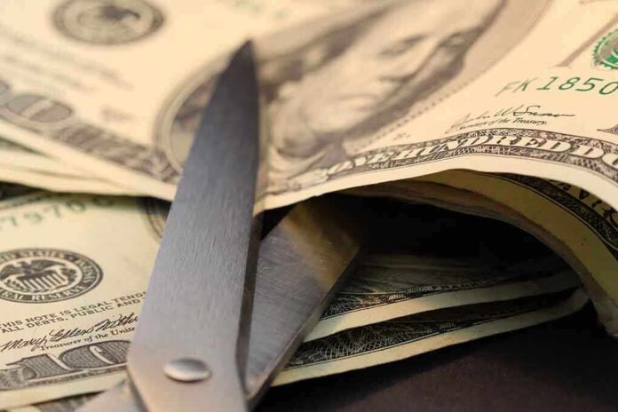 shutterstock_96493568.jpg Scissors cutting through a stack of dollar bills