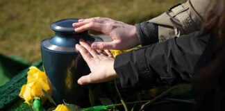 Hands touching an urn surrounded by yellow roses.
