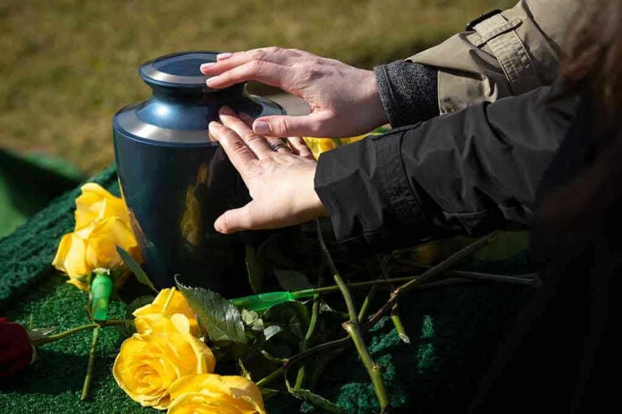 Hands touching an urn surrounded by yellow roses.