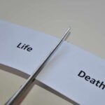 Scissors cutting a paper strip labeled 'Life' and 'Death'