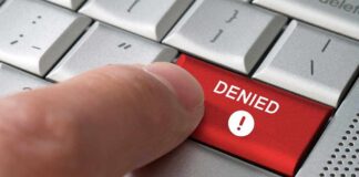 A finger pressing a red DENIED button on a computer keyboard
