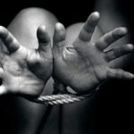 Two hands reaching out, bound by rope in a black and white image