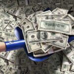 A shovel filled with stacks of cash on a background of scattered dollar bills