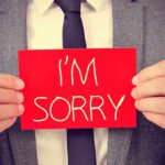 A man in a suit holding a red sign that says IM SORRY