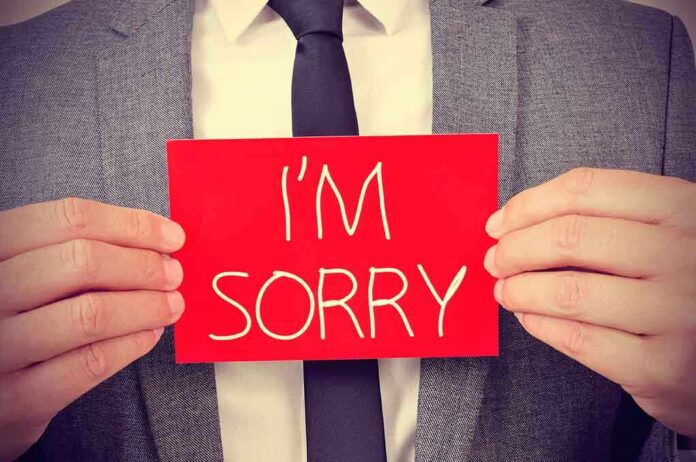 A man in a suit holding a red sign that says IM SORRY