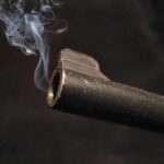 Close-up of a gun barrel emitting smoke against a black background