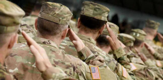 Soldiers in camouflage uniforms saluting in formation outdoors