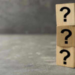 Three wooden blocks with black question marks stacked.